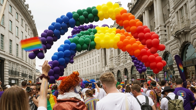 Rainbow-coloured balloons float above a parade of people during Pride in London.