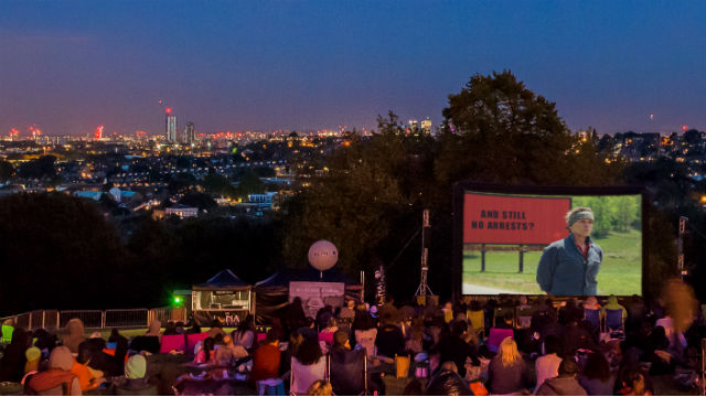People at an outdoor cinema screen with Luna Cinema at Alexandra Palace in London at dusk.