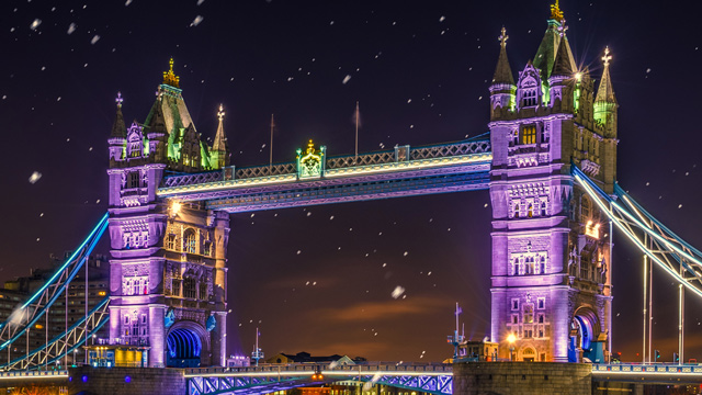 Tower Bridge lit up at night in purples and yellows.