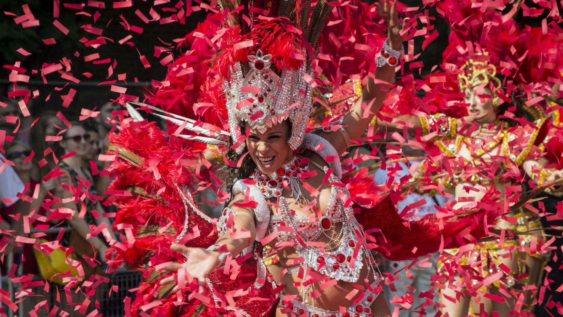 A Notting Hill Carnival performer dances surrounded by red confetti.