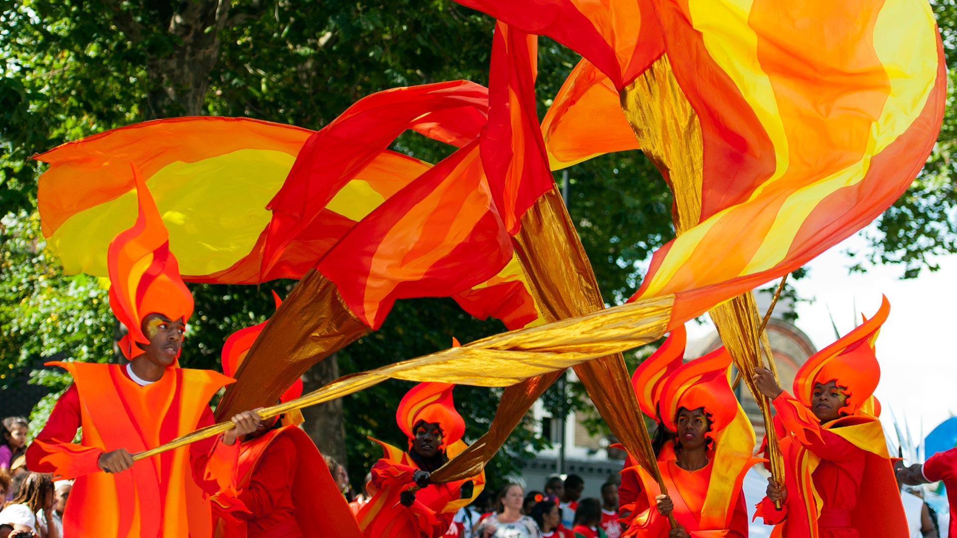 A group of performers swirls orange, yellow and red banners in the air during Notting Hill Carnival.