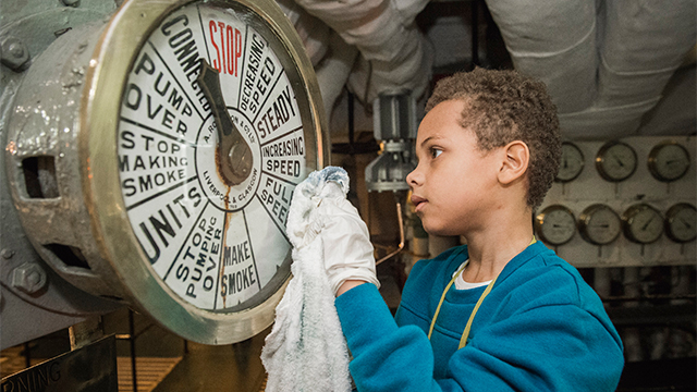 A boy helps to clean a gauge on HMS Belfast, as part of the Ship Shape activities. 