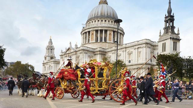 Un carrosse doré, conduit par des personnes en livrée rouge traditionnelle, passe devant la cathédrale Saint-Paul.