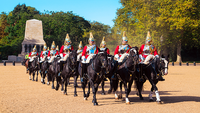 The Household Cavalry soldiers, dressed with the traditional red tunique, breast plates and plumed helmets, are performing a ceremony on Horseguards parade.