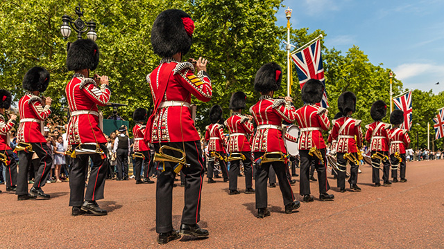 Guards, dressed in red tunics with black bearskin hats, play instruments as they march along The Mall towards Buckingham Palace.