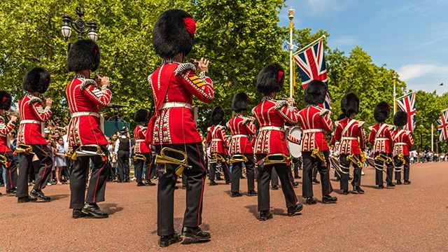 Trooping the Colour © Shutterstock Guards, dressed in red tunics with black bearskin hats, play instruments as they march along The Mall towards Buckingham Palace.