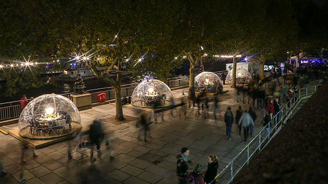 A night-time panoramic view of clear plastic domes "snow globes", with tables and chairs inside, along the South Bank.