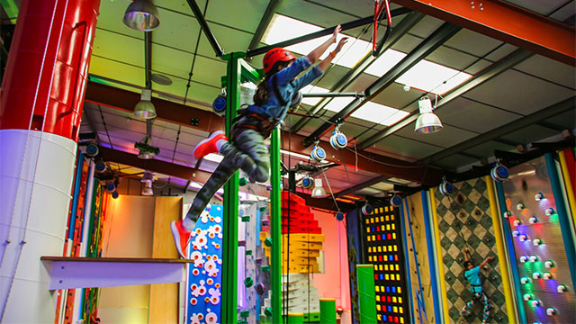 A child jumping from a platform and reaching for the bar at the Leap of Faith climbing challenge at Clip 'N Climb in Chelsea