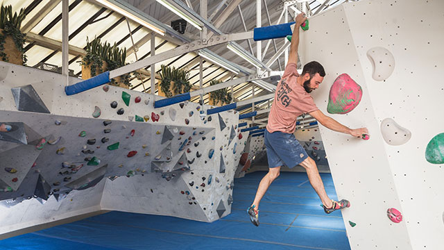 A man in a pink t-shirt and shorts climbing the wall at The Arch Climbing Wall in Bermondsey.