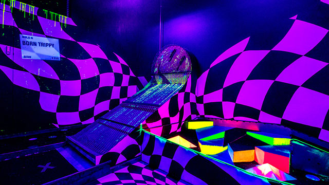 A neon purple golf obstacle with multi-coloured light boxes and a wall covered with black and purple checks in the background