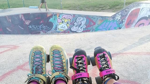 Two skaters wearing colourful yellow and pink roller skates sitting by a concrete skatepark covered in graffiti.