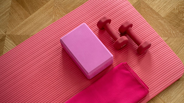 A pink yoga mat with a pink towel, pink weights and a pink yoga block on the floor