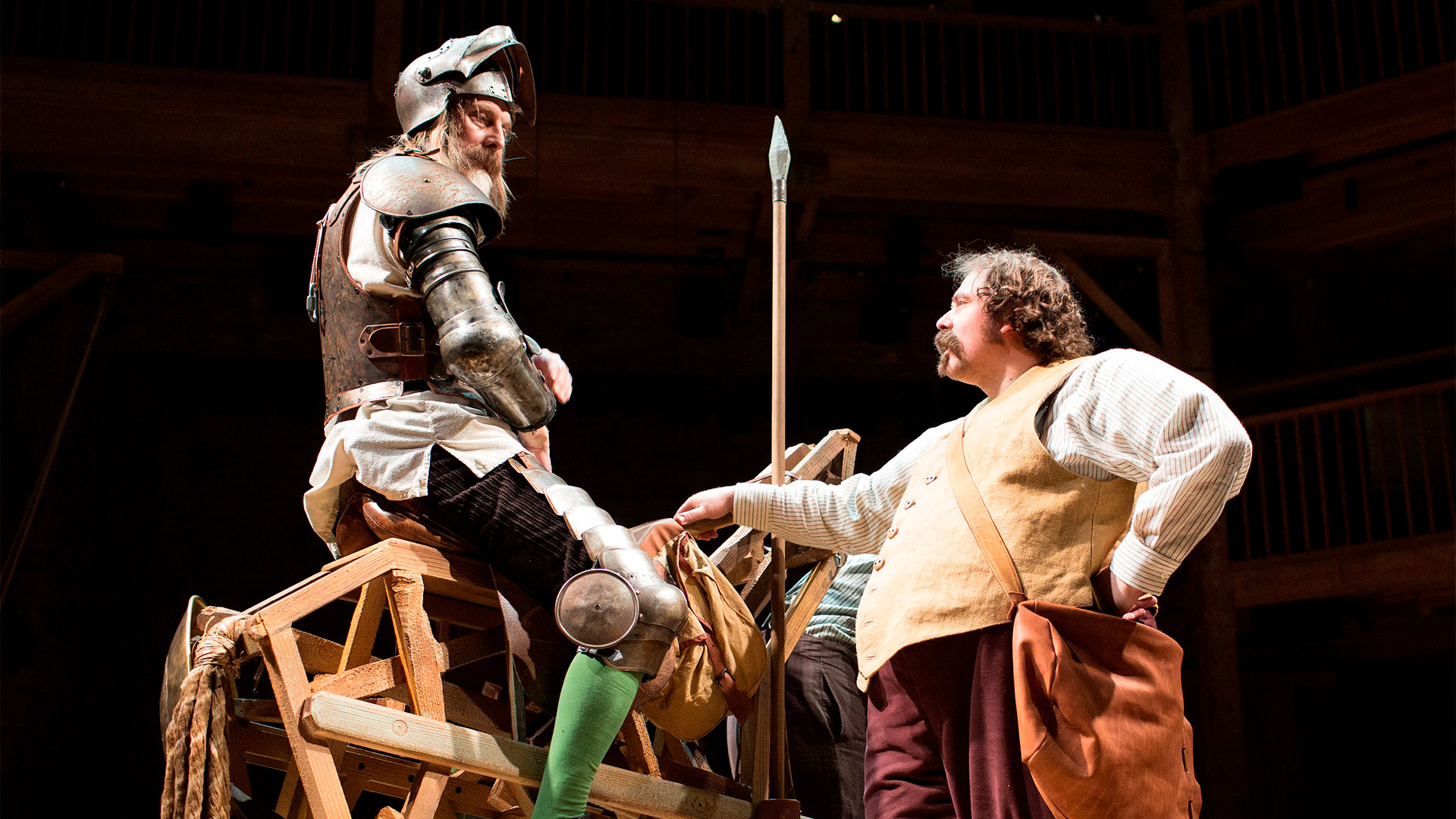 Dressed in armour, David Threlfall sits on a wooden horse as Rufus Hound stands below, leaning against the horse.