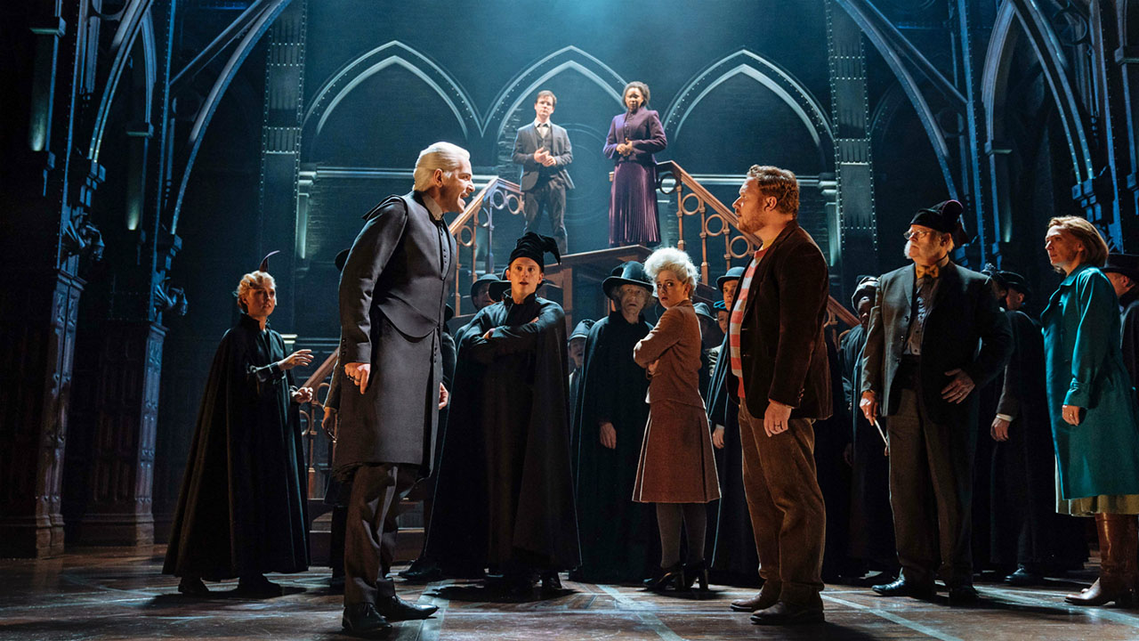 Scène de la production de Harry Potter et l'Enfant Maudit. Au premier plan Ron Weasley et Draco Malfoy s'affronte au milieu du personel au Ministere de la Magie. A l'arrière plan Harry Potter et Hermione Granger observent la scène.