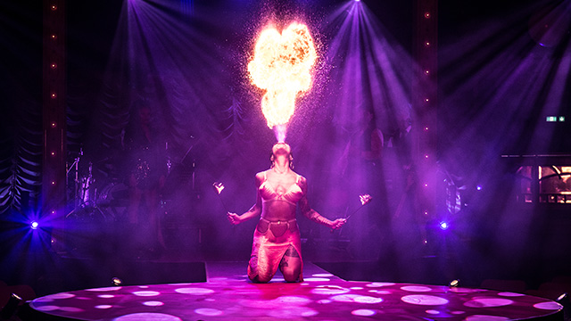 A person breathing fire into the air during a performance of La Clique.