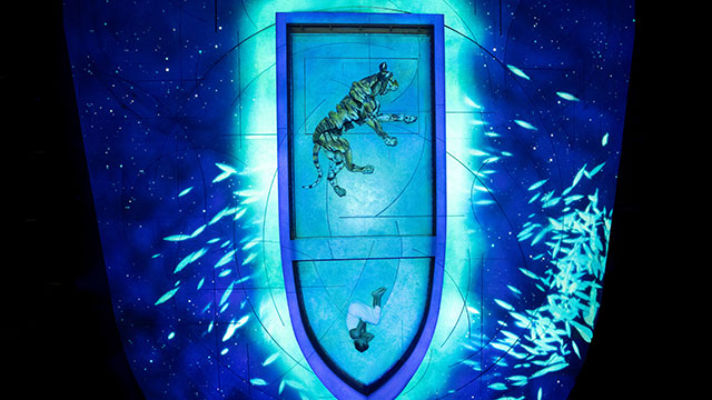 Un bateau de couleur bleu clair navigue une mer bleue foncée avec un garçon et un tigre à l'intérieur, au milieu de la nuit.