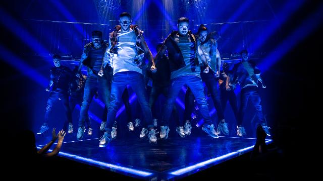 a group of dancers jump in the air with blue light projected on stage.