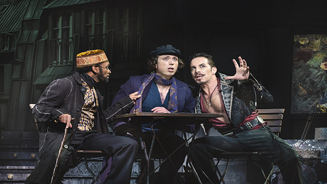 Trois hommes sont assis autour d'une table pour débattre de certaines idées sur la scène de Moulin Rouge au Picadilly Theatre.