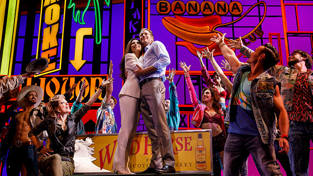 Edward and Vivian embrace centre stage in front of neon signs with the Pretty Woman cast raising their arms up to them. 