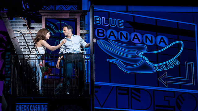 The two main characters of Pretty Woman, Vivian and Edward, are standing on the outside staircase of a building and next to the blue neon sign of a jazz club.