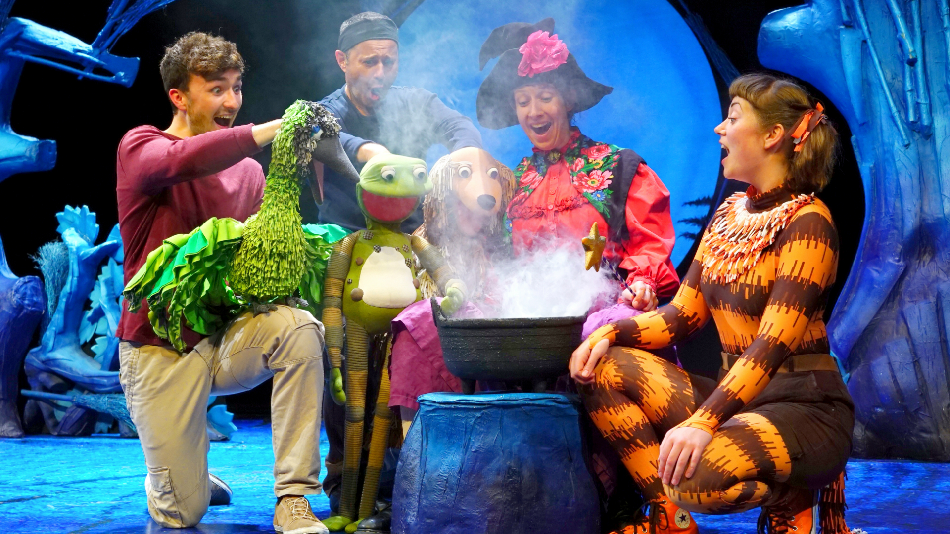 Room on the Broom Live at the Lyric Theatre. Image courtesy of Raw PR. A puppet bird, frog and dog sit around a smoking cauldron with actors dressed as a witch and a cat.