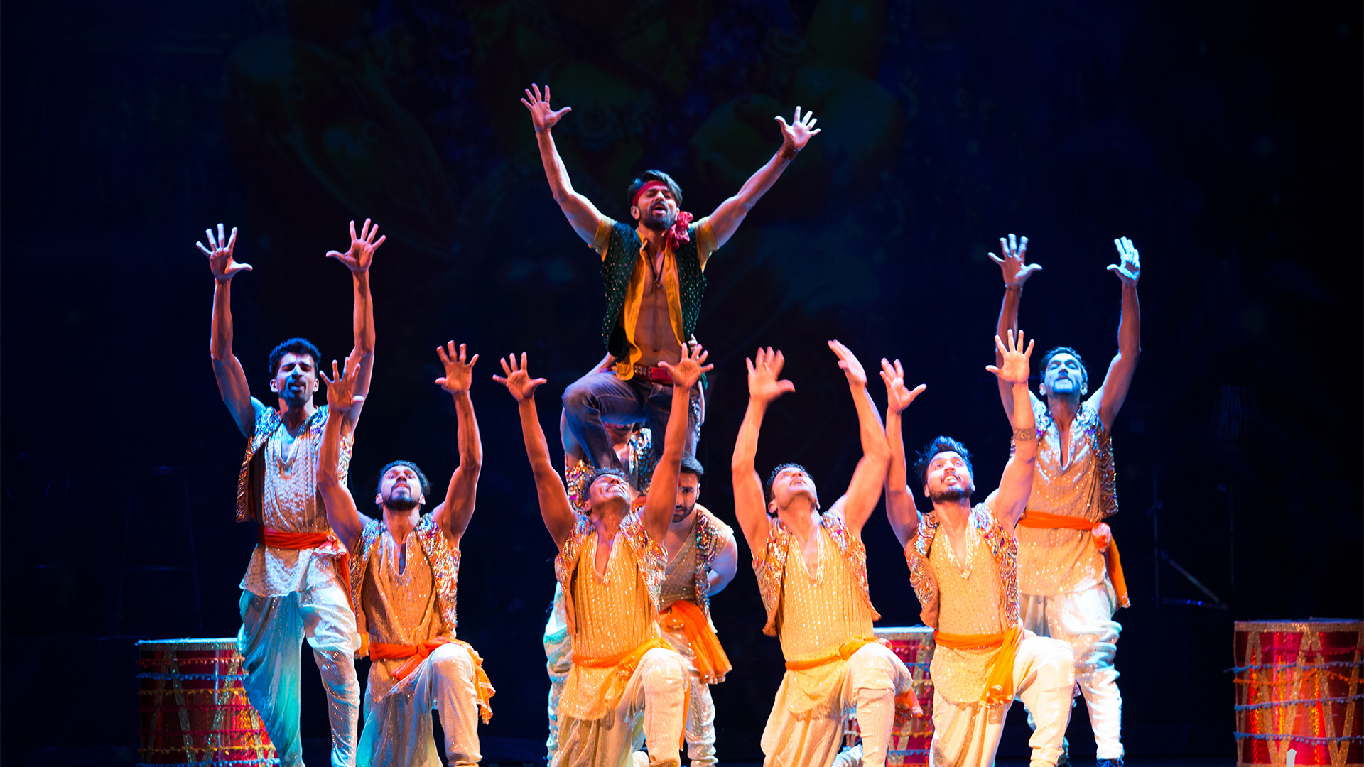 A group of 7 dancers hold their hands in the air during a performance of Taj Express.