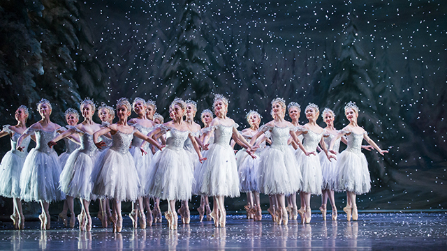 un groupe de danceuses de ballet portant des tutus blancs se trouve sur scène avec de la neige tombant du ciel. 