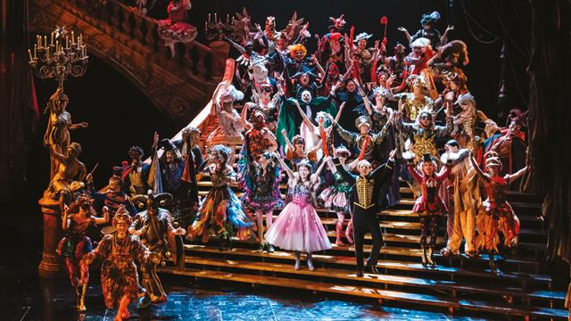 The cast of phantom of the opera dancing on the stairs on stage.