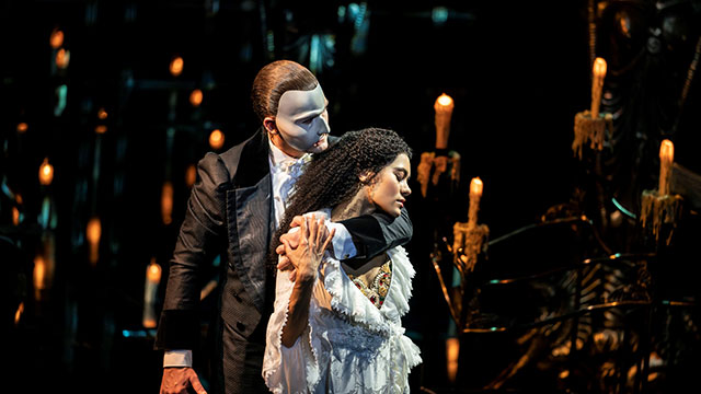 The cast of The Phantom of the opera on stage wearing colourful costumes and masks.