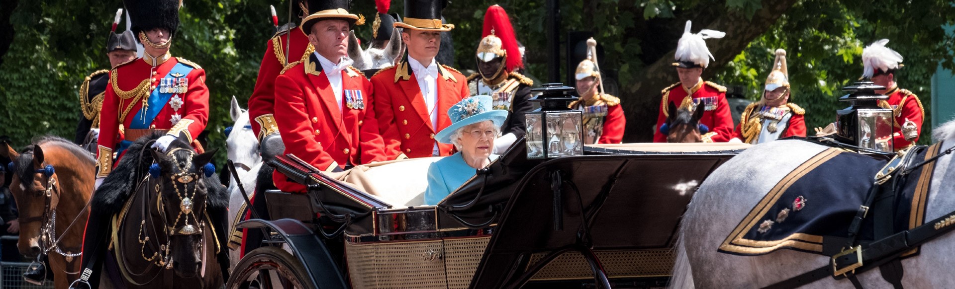 Queen Elizabeth II travels along The Mall in an open carriage pulled by horses, on her way from Buckingham Palace on a sunny day