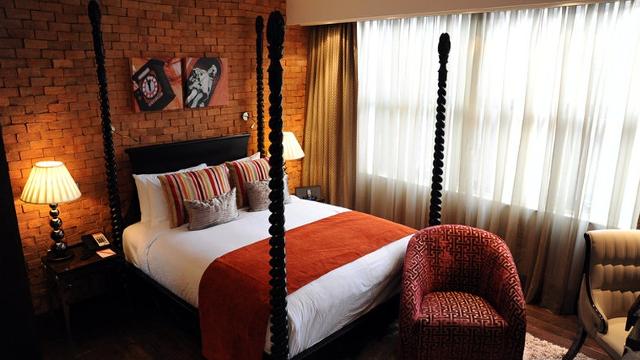 Современная кровать с балдахином у голой кирпичной стены с лампой с подсветкой на прикроватной тумбочке.