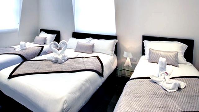 Three beds with white linen, black and grey throws and towels in the shape of swans.