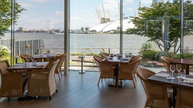 The restaurant at Radisson Blu Edwardian New Providence Wharf Hotel, London, with floor-to-ceiling windows looking out onto the river Thames and The O2 in the background.