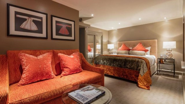 A room at Radisson Blu Edwardian Sussex Hotel, London, including an orange sofa, coffee table and a bed with white and orange bedding.