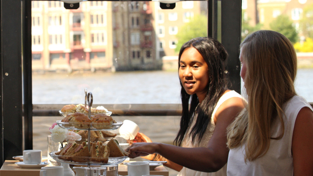 Two people sitting in a City Cruises boat with sandwiches and scones on the table.